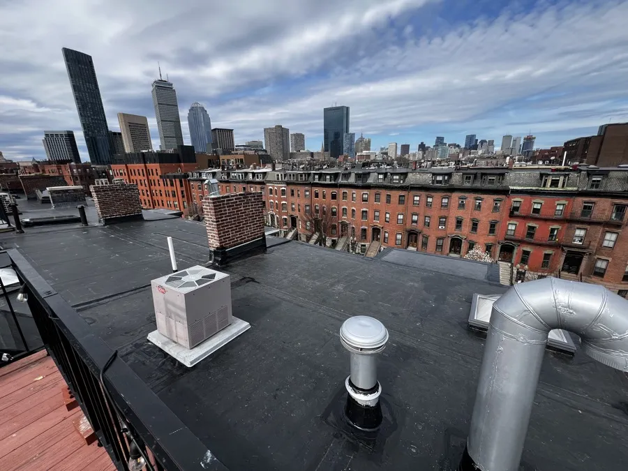 Rooftop view of brick chimneys with the Boston skyline in the background